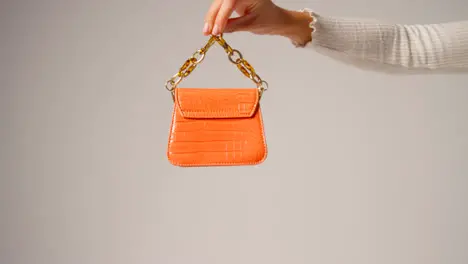 Close Up Of Female Social Media Influencer Producing User Generated Content Holding Out Orange Fashion Handbag 3