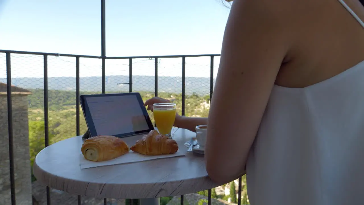 Young female entrepreneur working while eating her breakfast on the hotel balcony