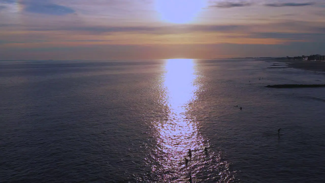 high up dolly shot forward descend over surfers in the Atlantic Ocean drone camera moving towards a golden sunset