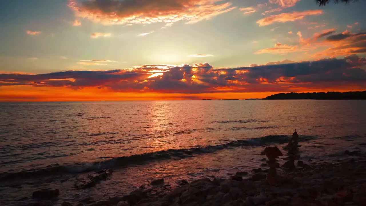 Cinemagraph seamless video loop of of the sun setting over the horizon at a romantic beach with small waves at the Croatian Mediterranean seaside with stone towers and ships passing by