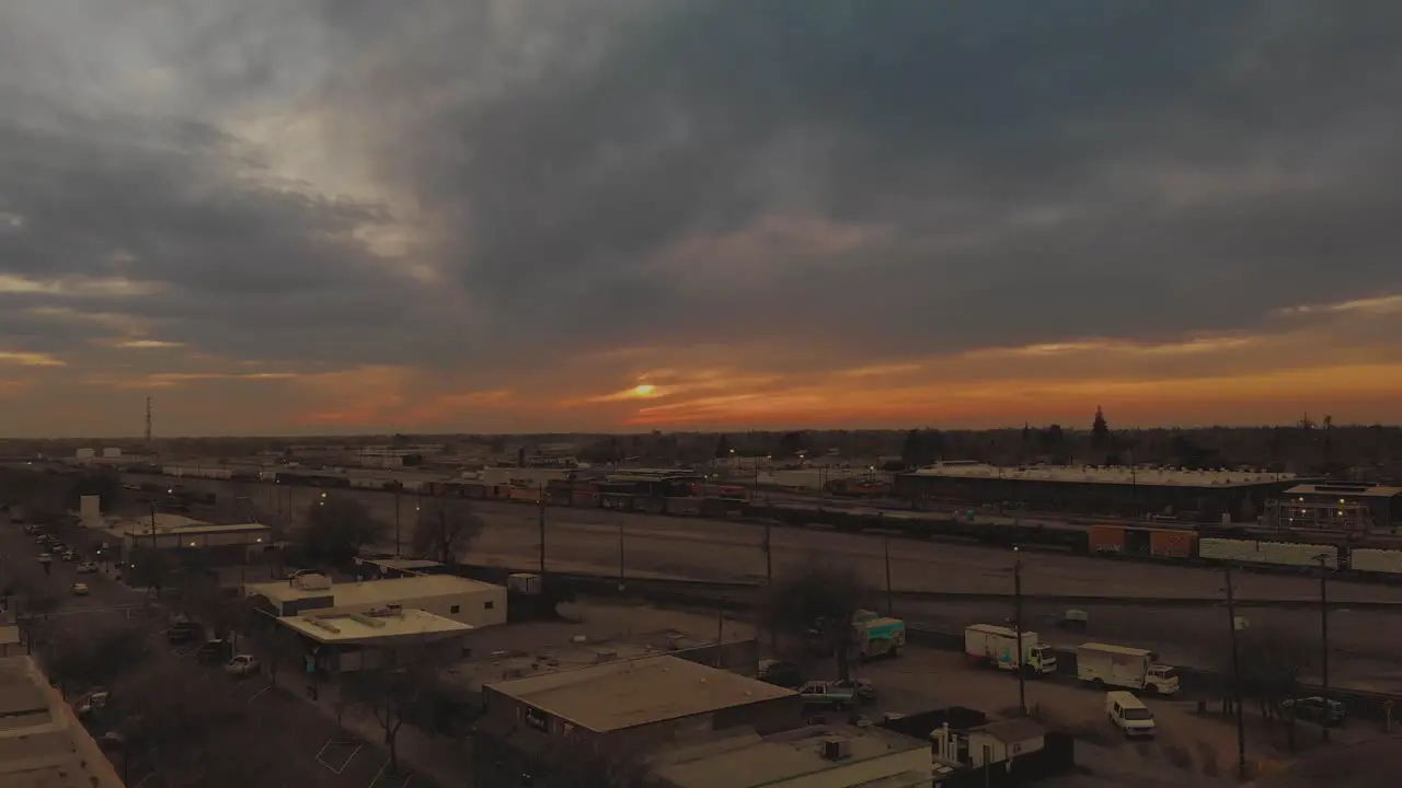 Cinematic top city aerial view of downtown Roseville California with industrial buildings shops and cargo train passing down the railroad with a vivid orange pink sunset in background