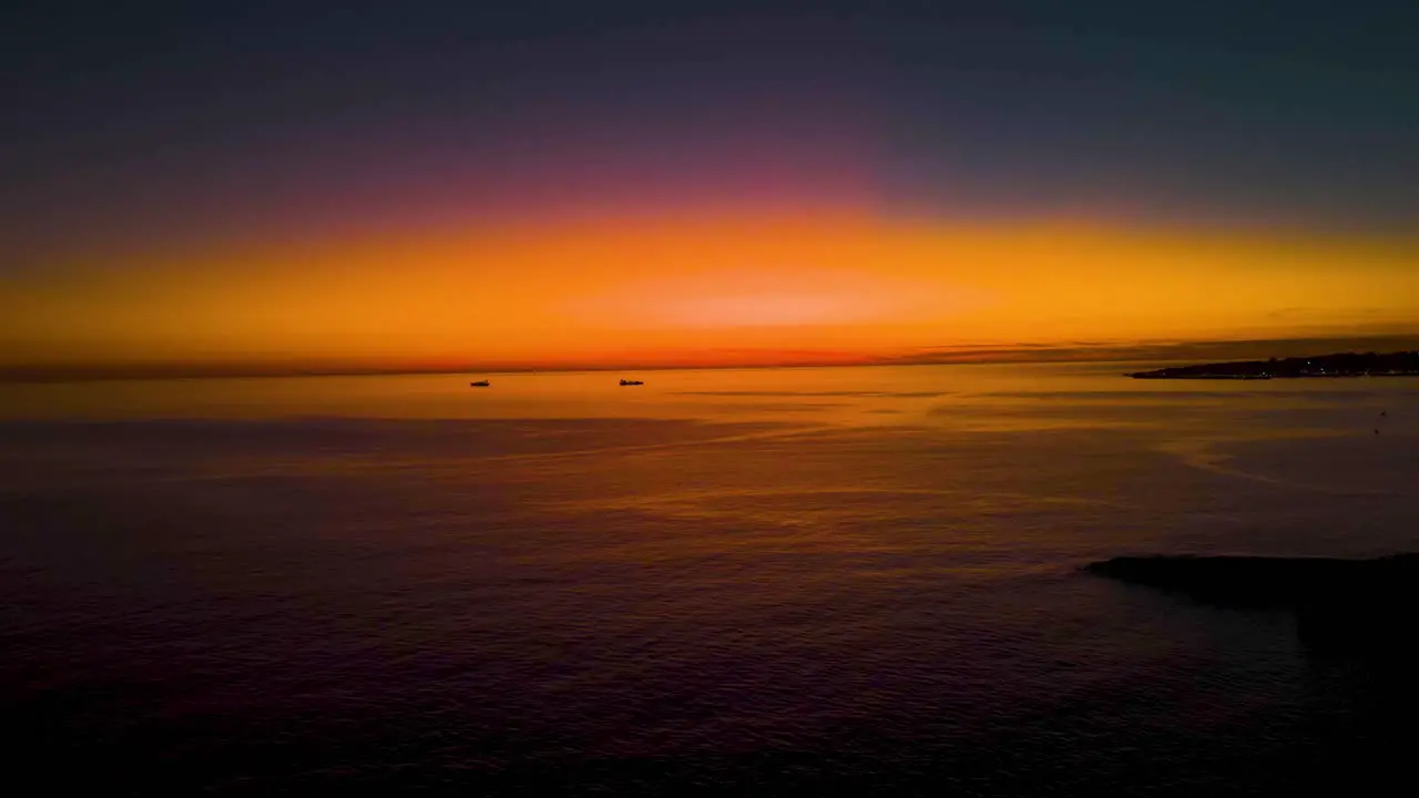 Amazing yellow and orange sky after sunrise reflected on sea surface with some boats sailing in Cascais