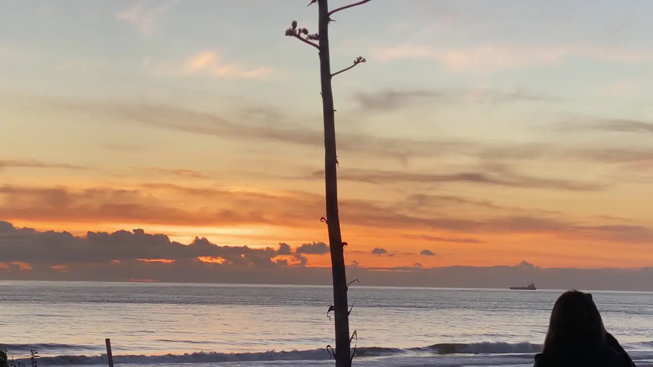 Silhouette of huge sunset with woman takes photos or video at sunrise on the beach