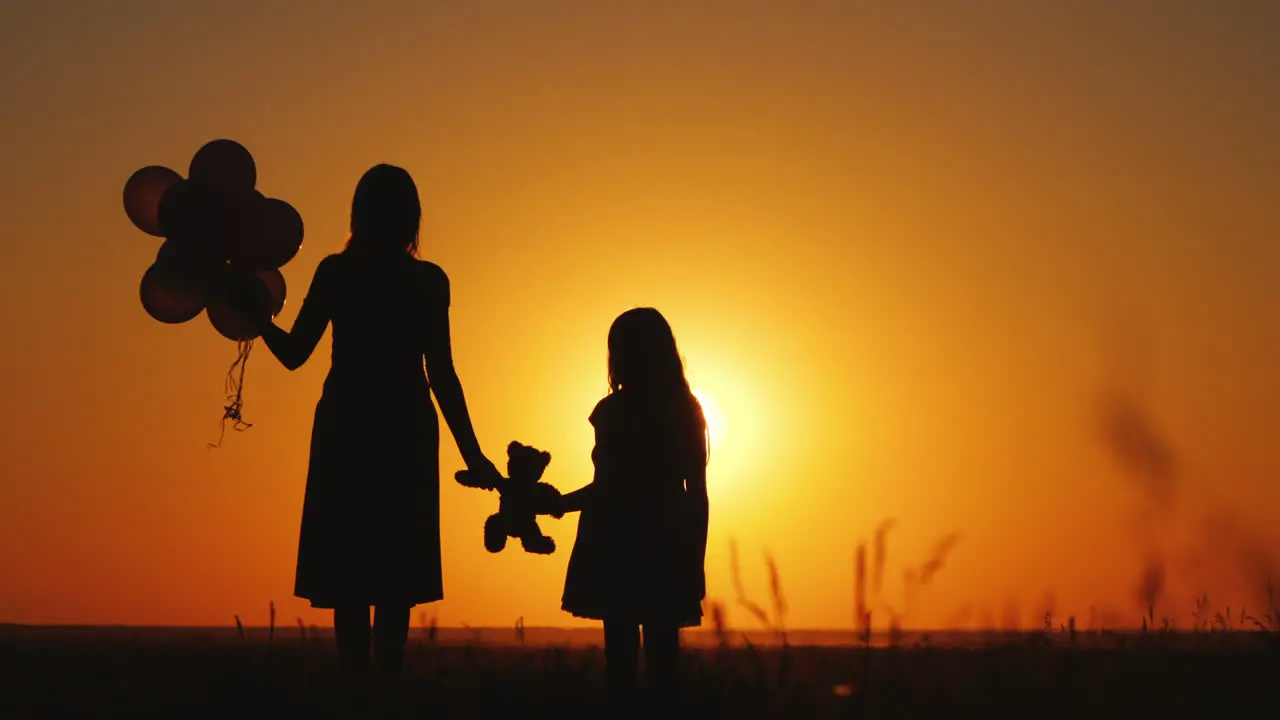 Mom And Daughter Admire The Sunset Hold Balloons And A Teddy Bear