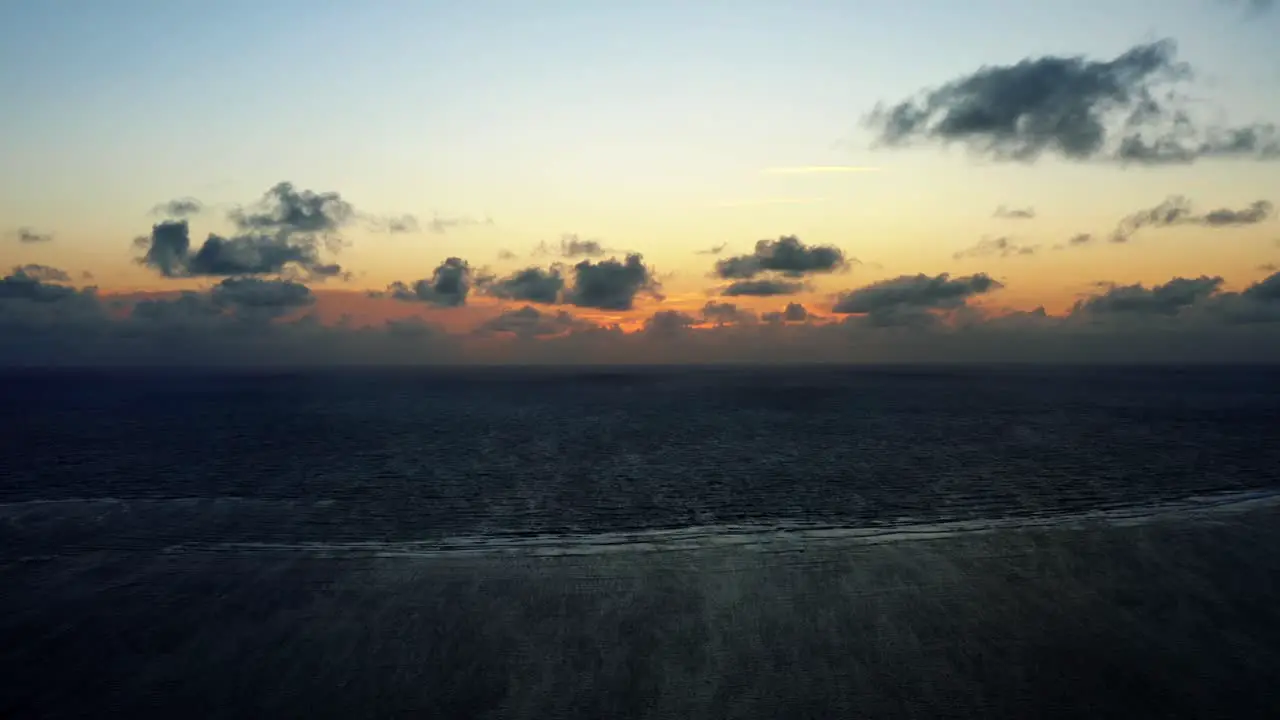 Beautiful wide aerial drone shot of a serene ocean sunrise at Well Beach near Joao Pessoa on a warm summer morning with the water below and golden clouds on the skyline