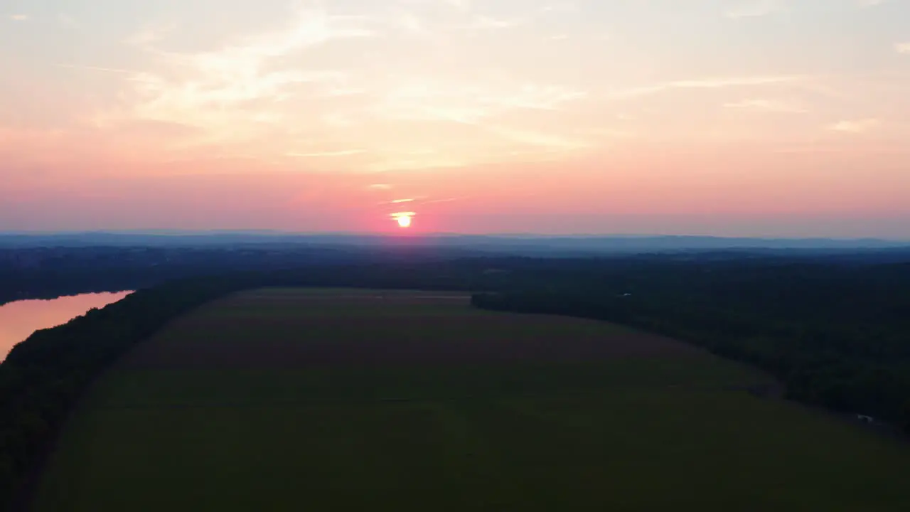 Beautiful pink orange sun peeks through the clouds and reflects of amazing Potomac River in Maryland surrounded by farms Drone Aerial