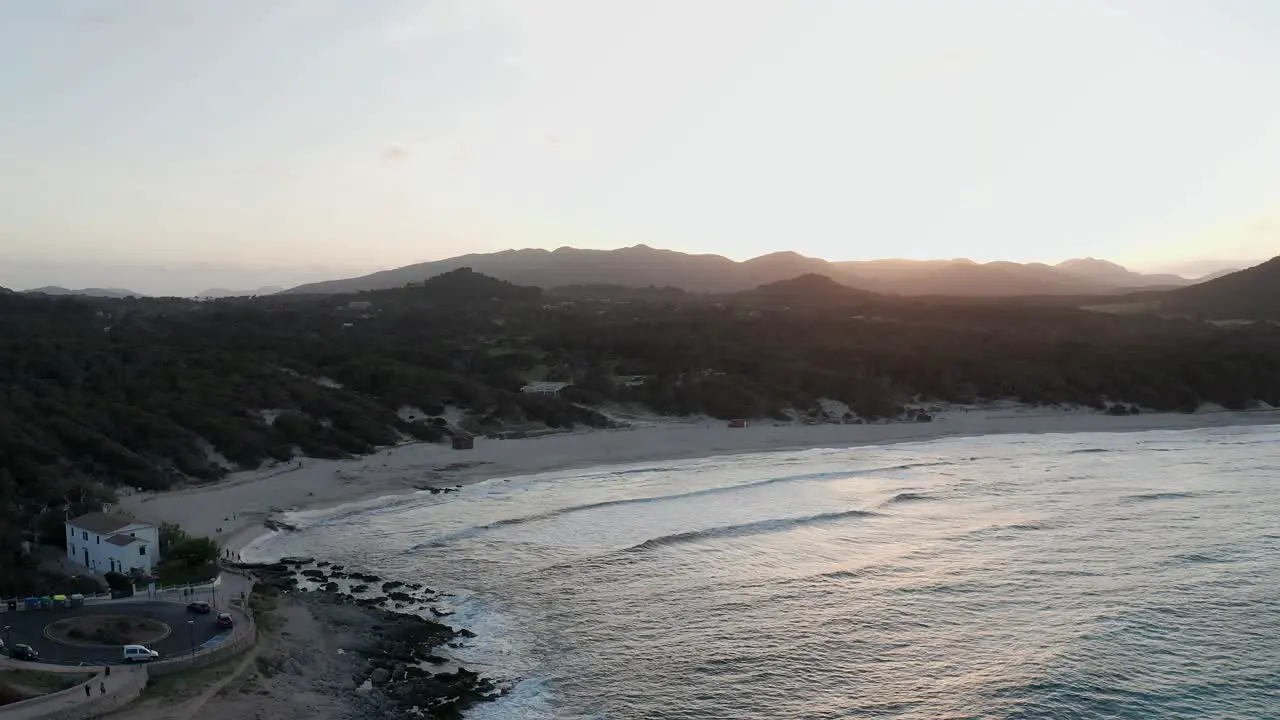 Mallorca beach Cala Aguila at sunset on a warm evening with waves crashing onto beach and the sun setting behind distant mountains