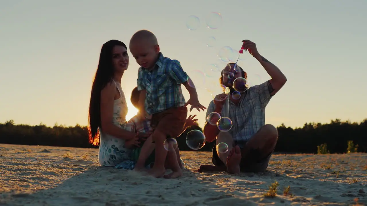 Parents Play With Two Boys At Sunset Blow Bubbles