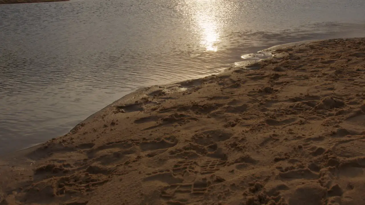 Tilt from footprints in the sand to sunset over water