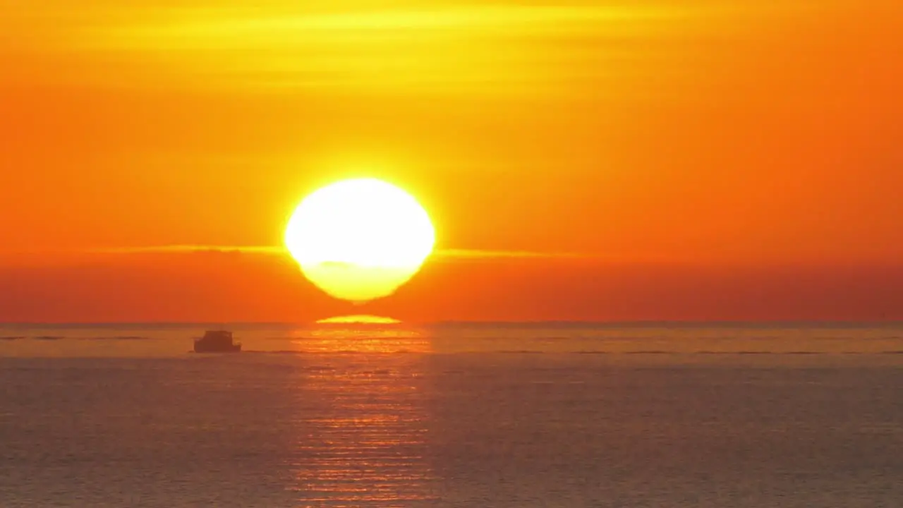 Fishing boat silhouette against orange sunrise over calm sea sun on horizon