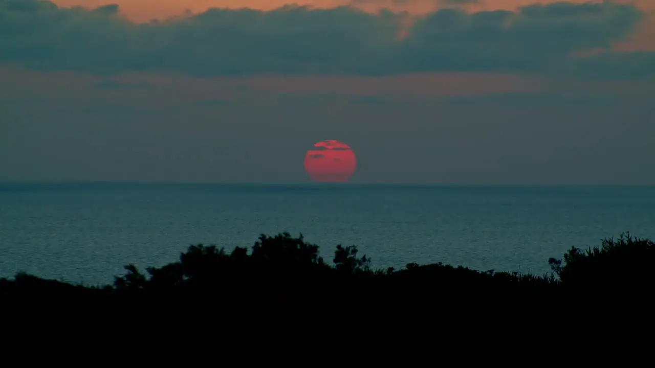 Astonishing red sun setting below sea horizon cumulus grey clouds static