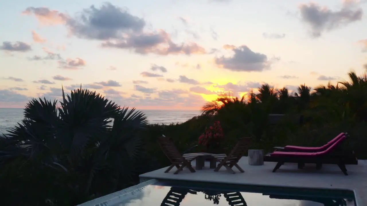 Drone flies over luxurious pool in private beachside ocean front villa and up towards the beach at sunset