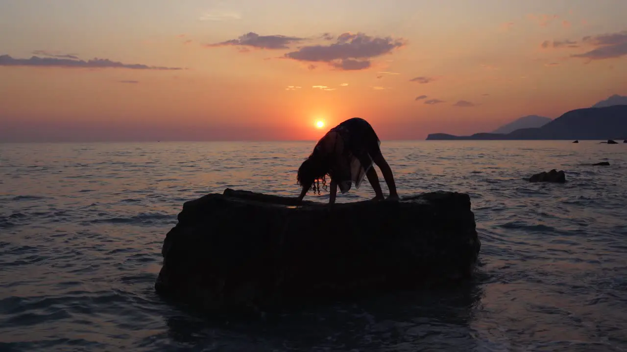 Yoga poses performed by young woman on cliffs of seashore at beautiful sunset