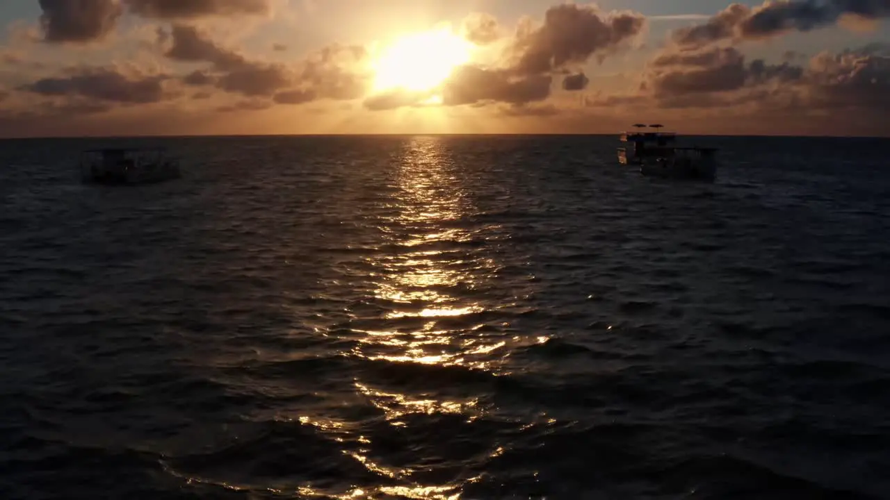 Beautiful aerial tilt up drone shot of an ocean sunrise at Well Beach near Joao Pessoa on a warm summer morning with the water below golden clouds on the skyline and small boats in the water