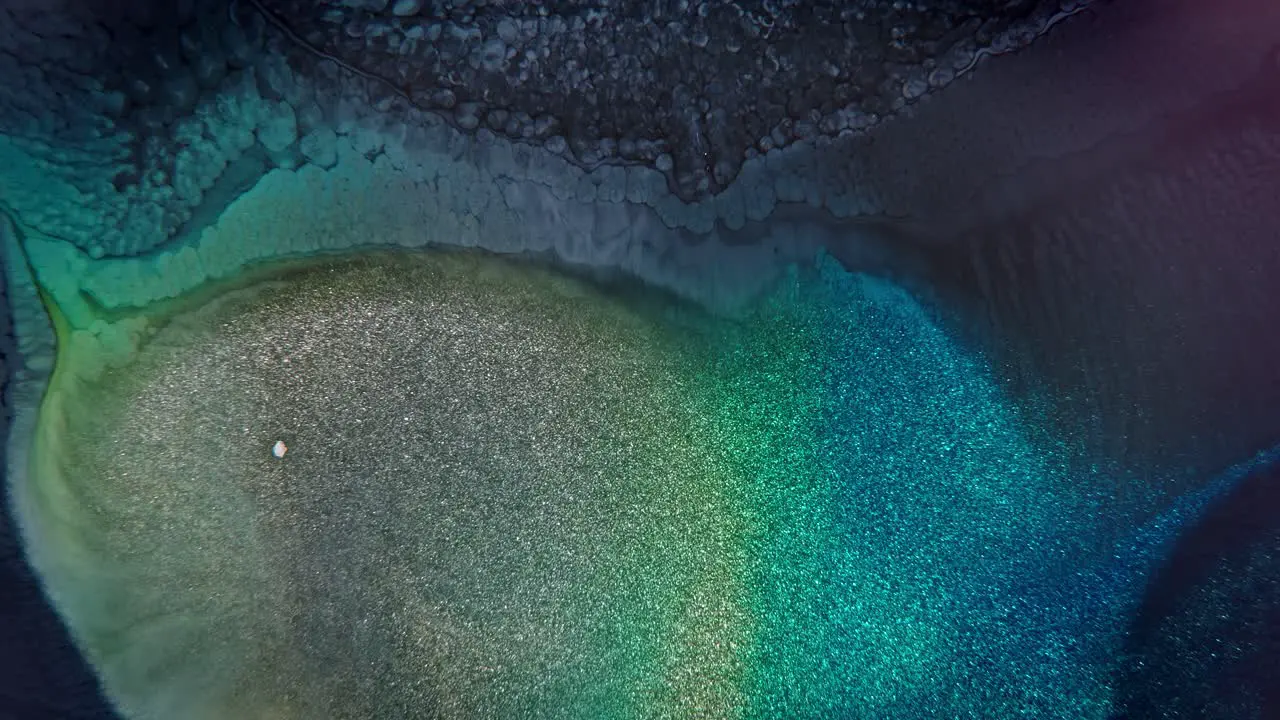 Close-up of blue and green ink granules on textured surface creating a sparkling underwater-like abstract effect