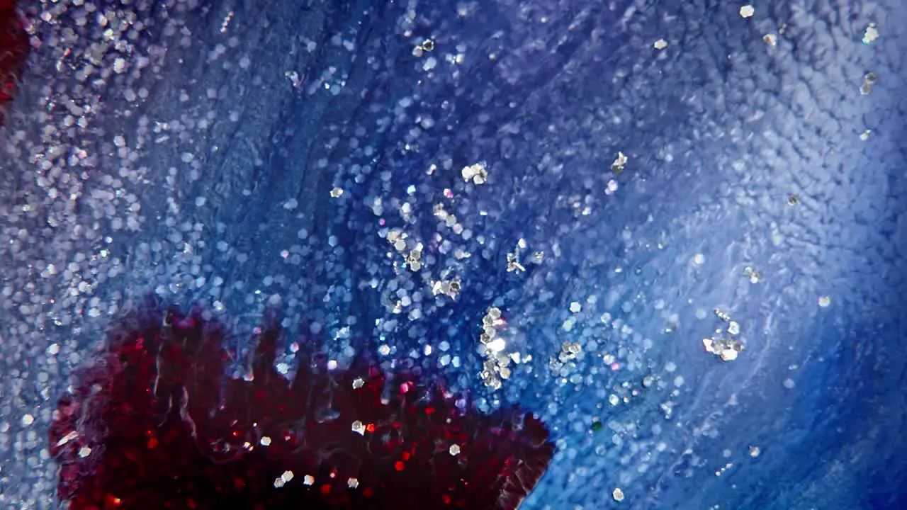 Blue and red ink dispersing in water with sparkling particles creating an abstract celestial background