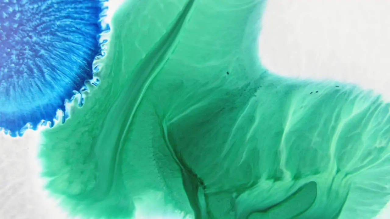 Close-up of vibrant blue and green ink patterns merging in water creating an abstract art effect