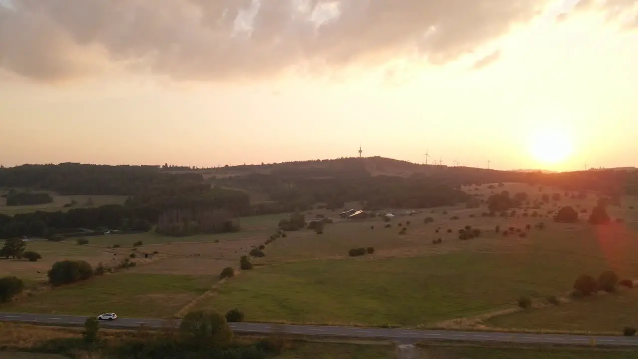 Dolly Aerial Shot Of The Sun Setting Behind A Small Hill Surrounded By Livestock