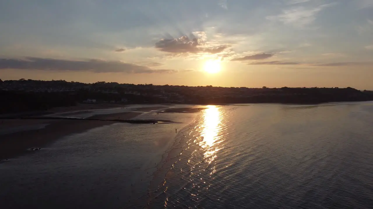 Sunset rays beam fiery golden colours across relaxing beach ocean coastline aerial view descend to above water