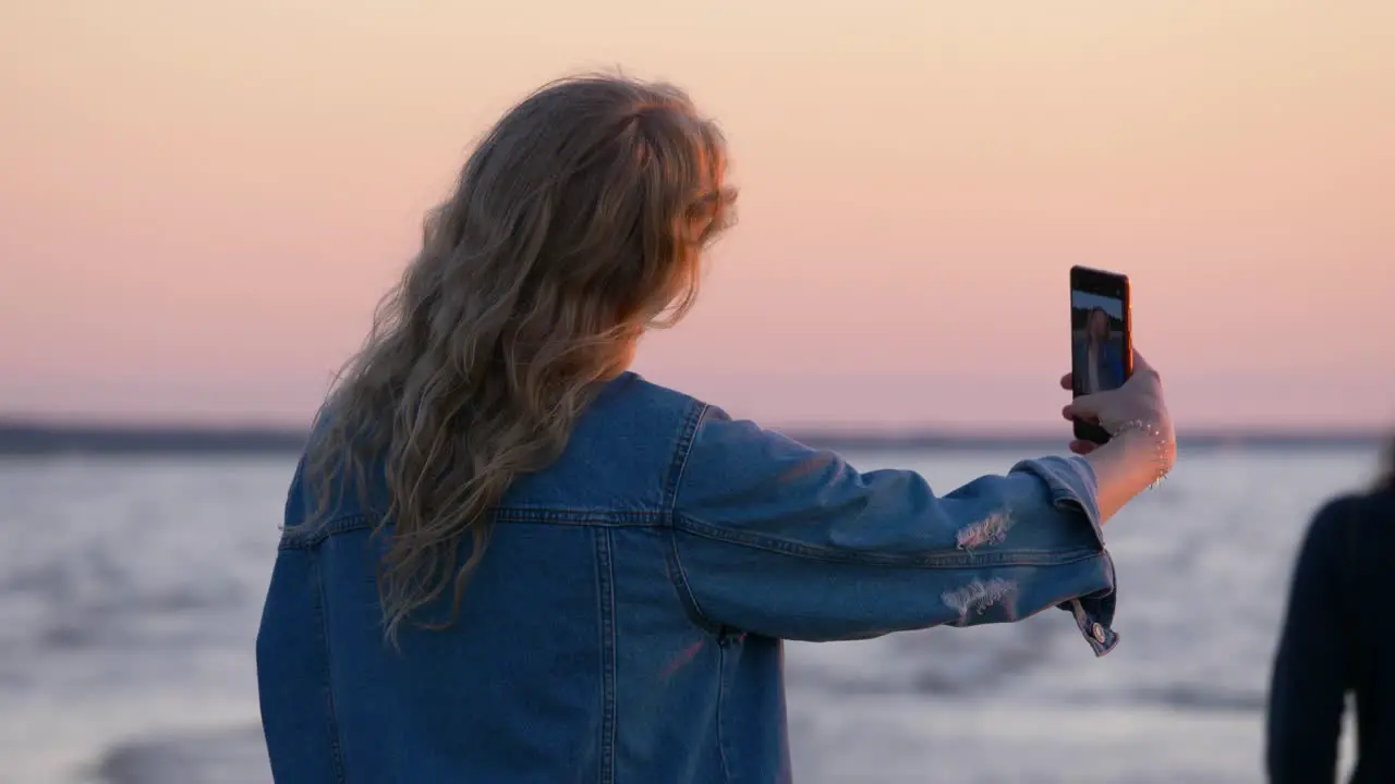 Shot from side how young beautiful woman takes a selfie near the sea