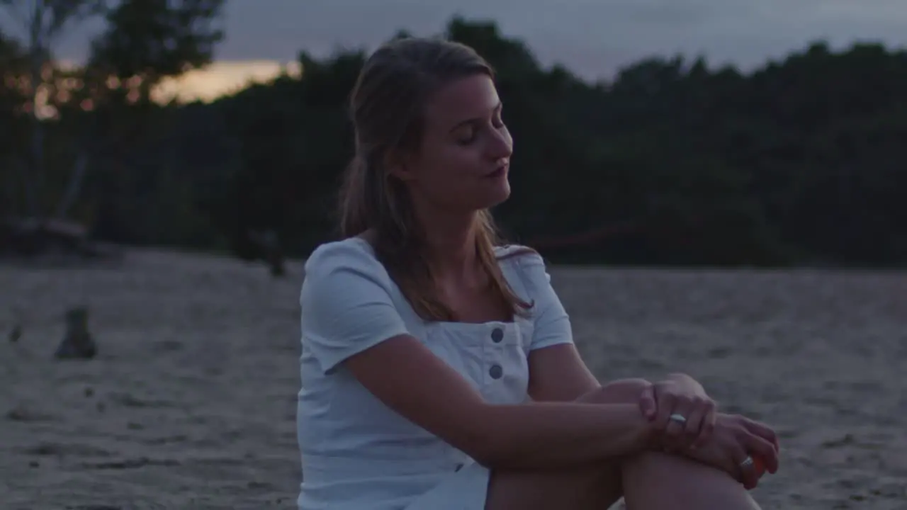 Attractive young woman sitting in sand dunes at dusk