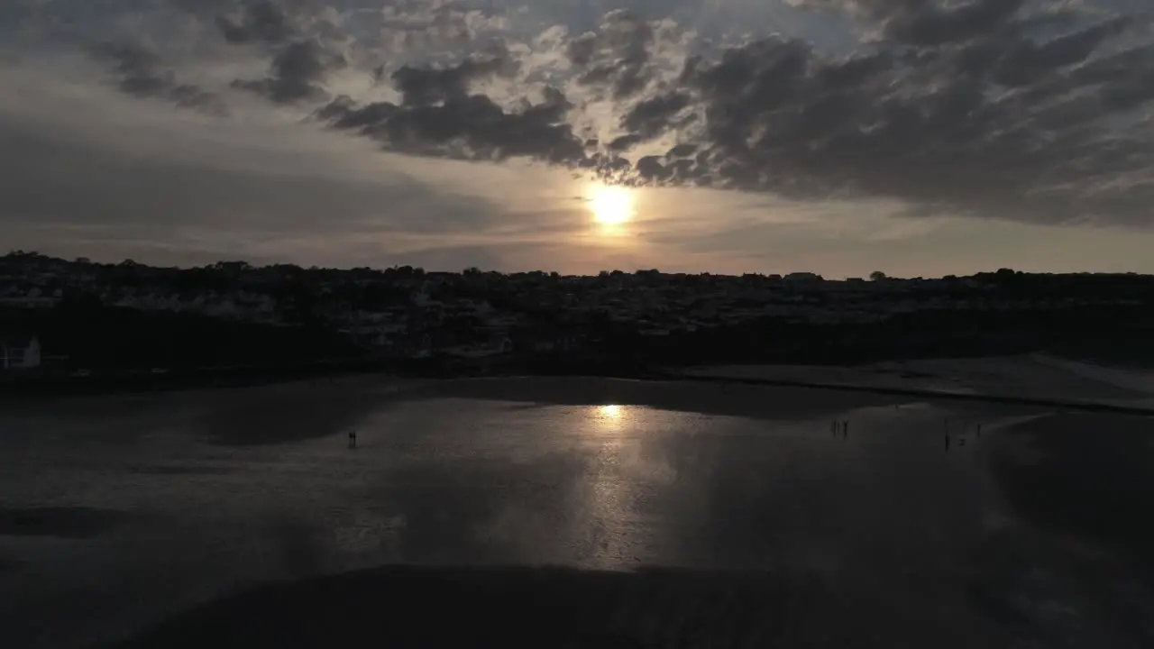 Evening cloudy golden sunset colours across Benllech beach silhouette coastline Anglesey aerial view slow rising forwards