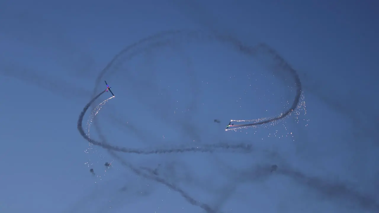 Tandem acrobatic pyrotechnical aircraft doing circular maneuvers in sync releasing sparks