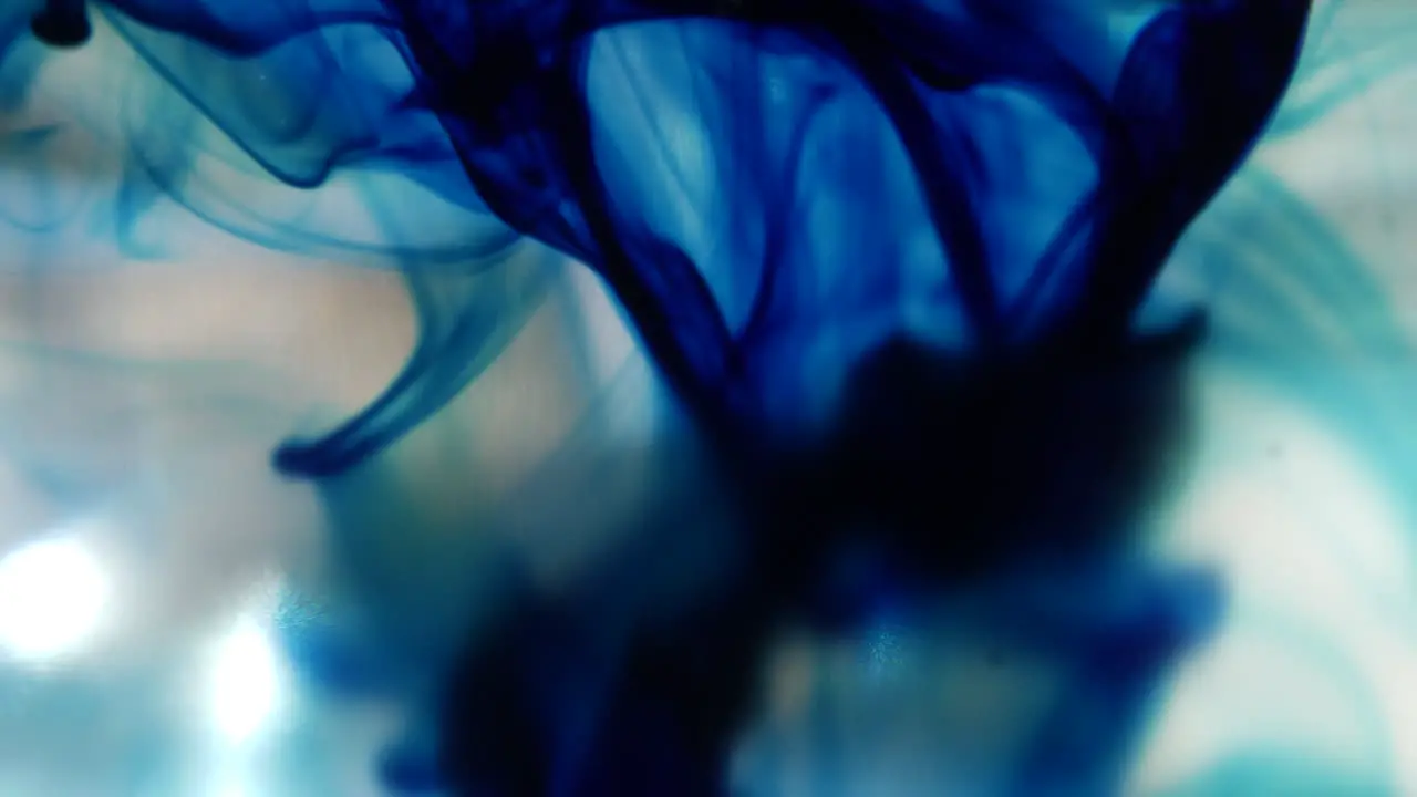 Macro shot of blue ink drops as it spreads out slowly underwater and creates smokey abstract shapes in the background