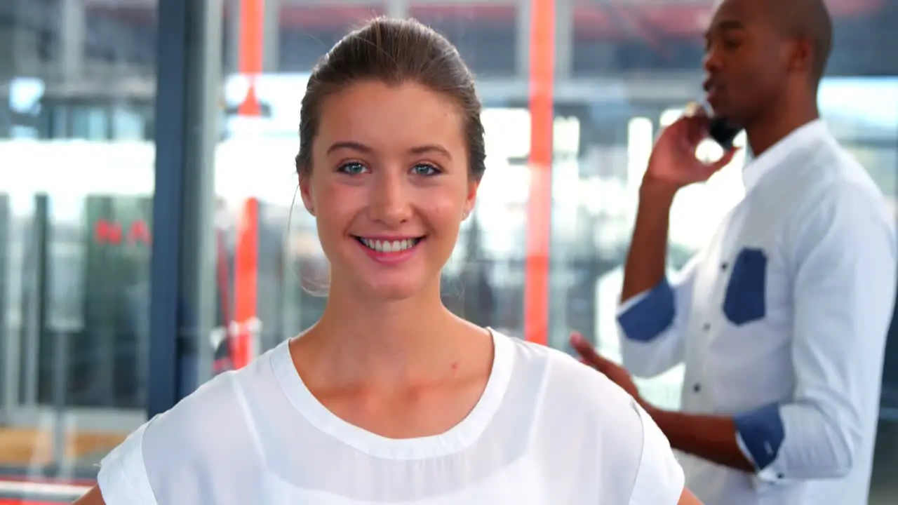 Female business executive smiling at camera while colleague talking on mobile phone