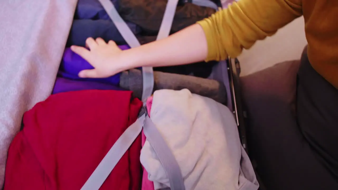 Lovely Asian woman making video call with family while preparing suitcases for clothes for travel