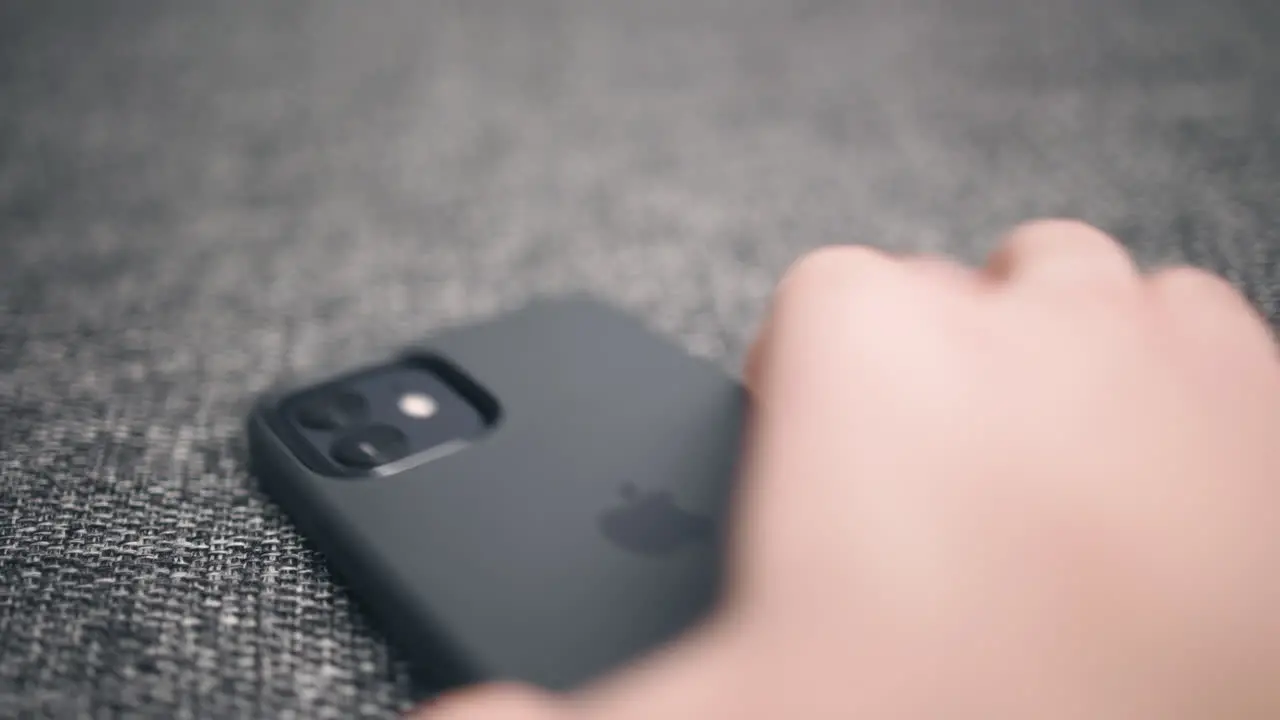 Close-up of hand picking up dark new iPhone from soft grey surface