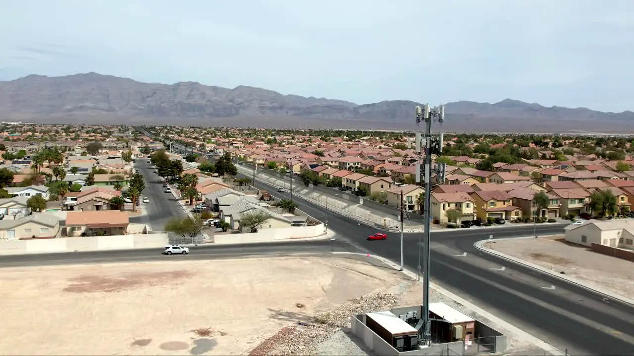 Cell tower on the foreground in a Las Vegas suburb with mountains beyond the valley ascending aerial view