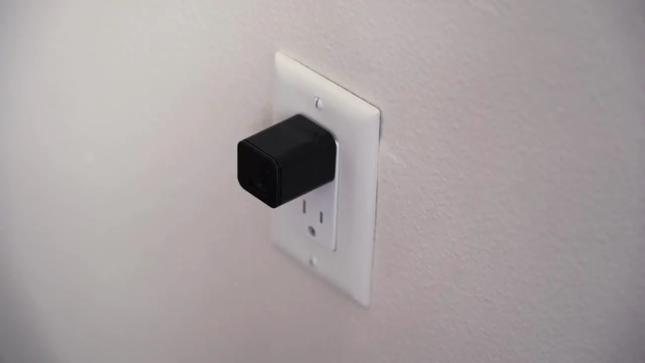 Woman plugs in a hidden camera that simulates a black cell phone charger cube