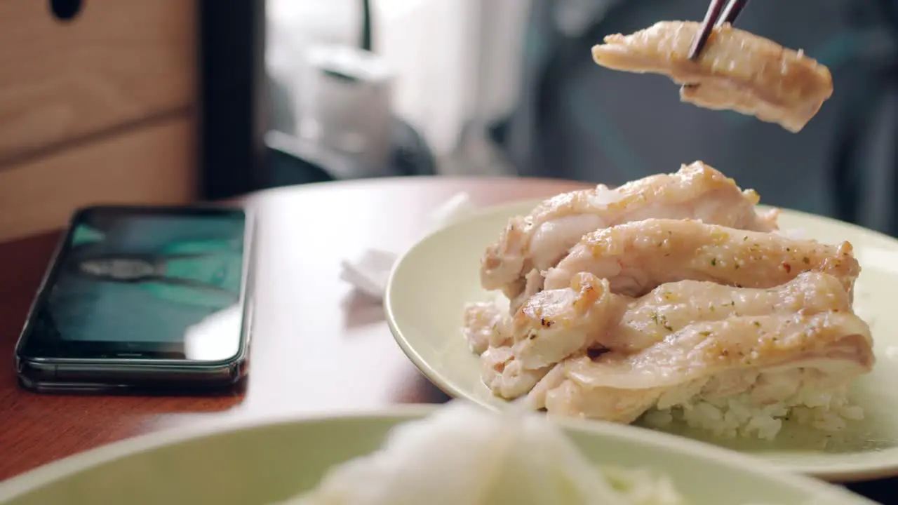 Person Watching Videos On Smartphone While Eating A Chicken Fillet On Rice