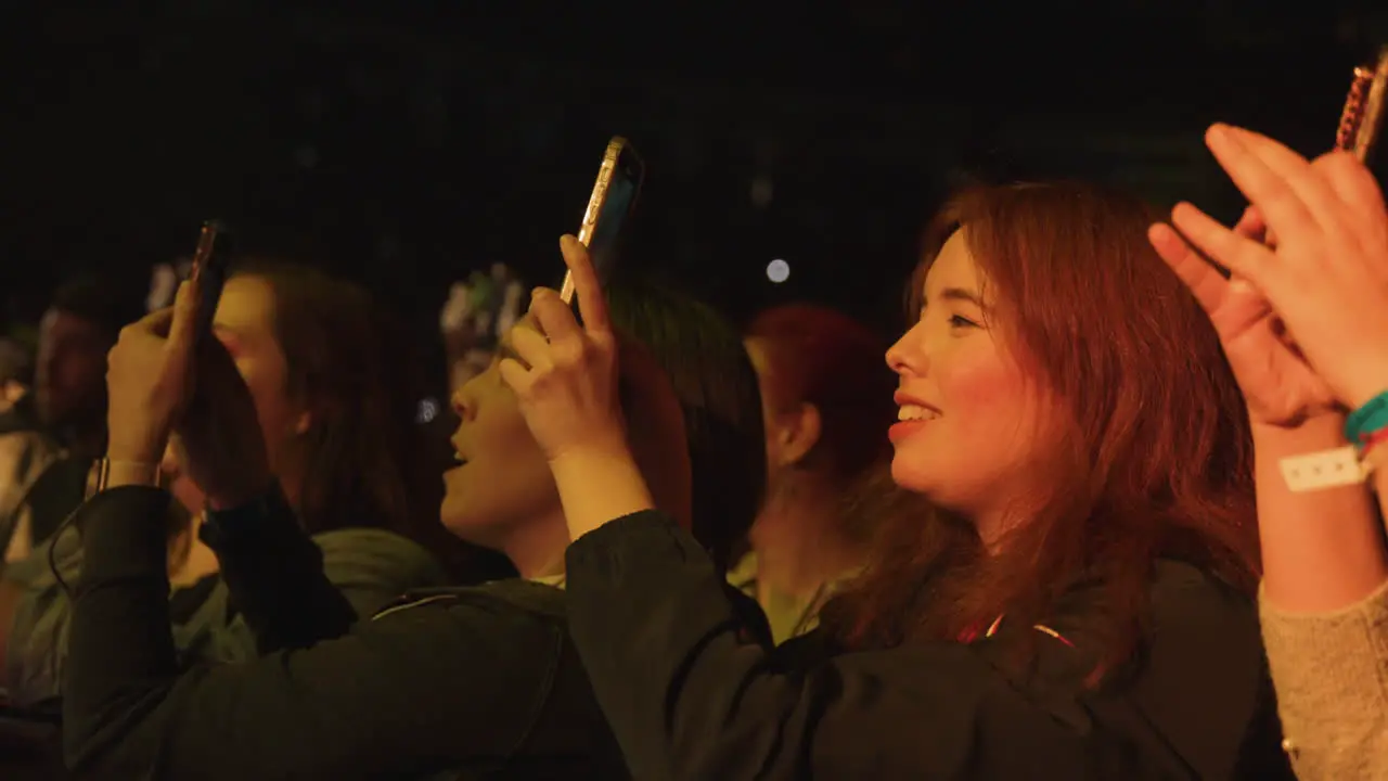 Young Women Ladies Holding Cell Phones Filming and Singing During Music Concert Show Audience Crowd in Arena Filming Music Performance on Stage