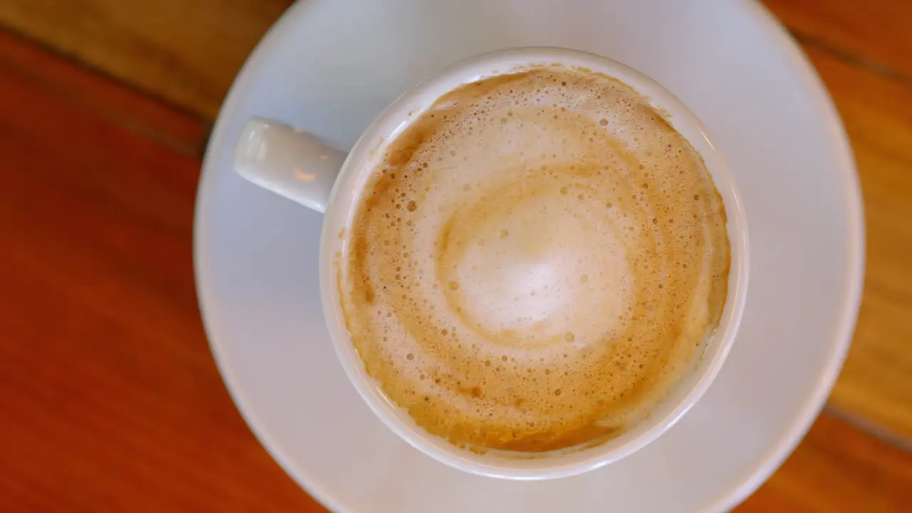 overhead video of a cup of cappuccino served in a white cup on a wooden table