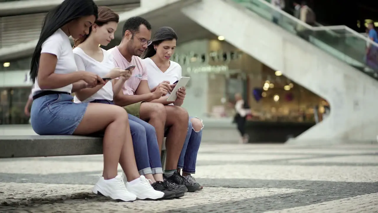 Calm people sitting on bench with modern devices