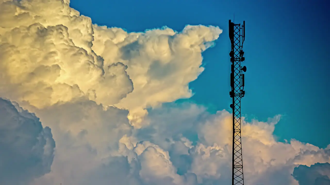 A cumulus cloud forms in a blue sky next to a cell phone tower