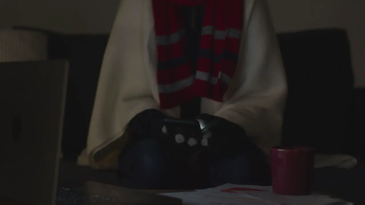 Person Wearing Blanket Using Phone Sitting On Sofa At Home When Power Is Cut Off