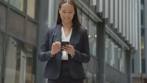 Businesswoman Walking Outside City Of London Offices Using Mobile Phone