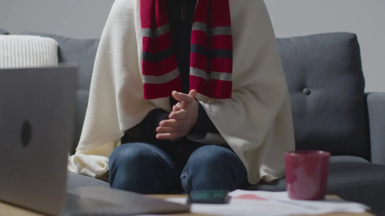 Person Wearing Blanket Sitting On Sofa At Home When Power Is Cut Off Using Phone Torch