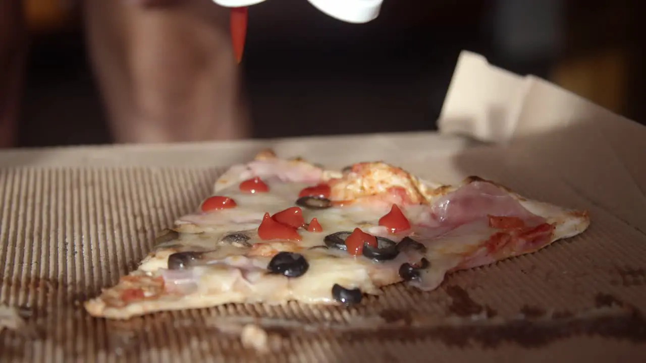 pouring ketchup on a pizza slice in a cardboard box close up slow motion