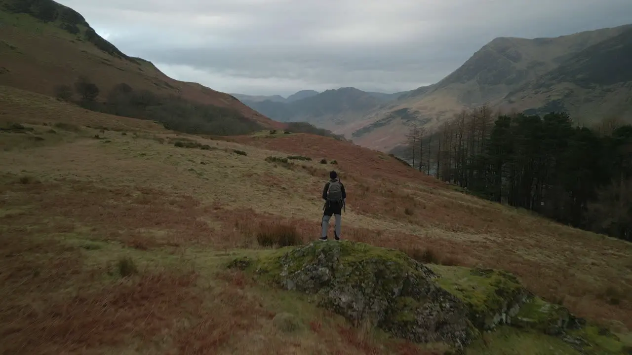 Flying past hiker on rocky outcrop towards distant misty mountains at Buttermere English Lake District UK