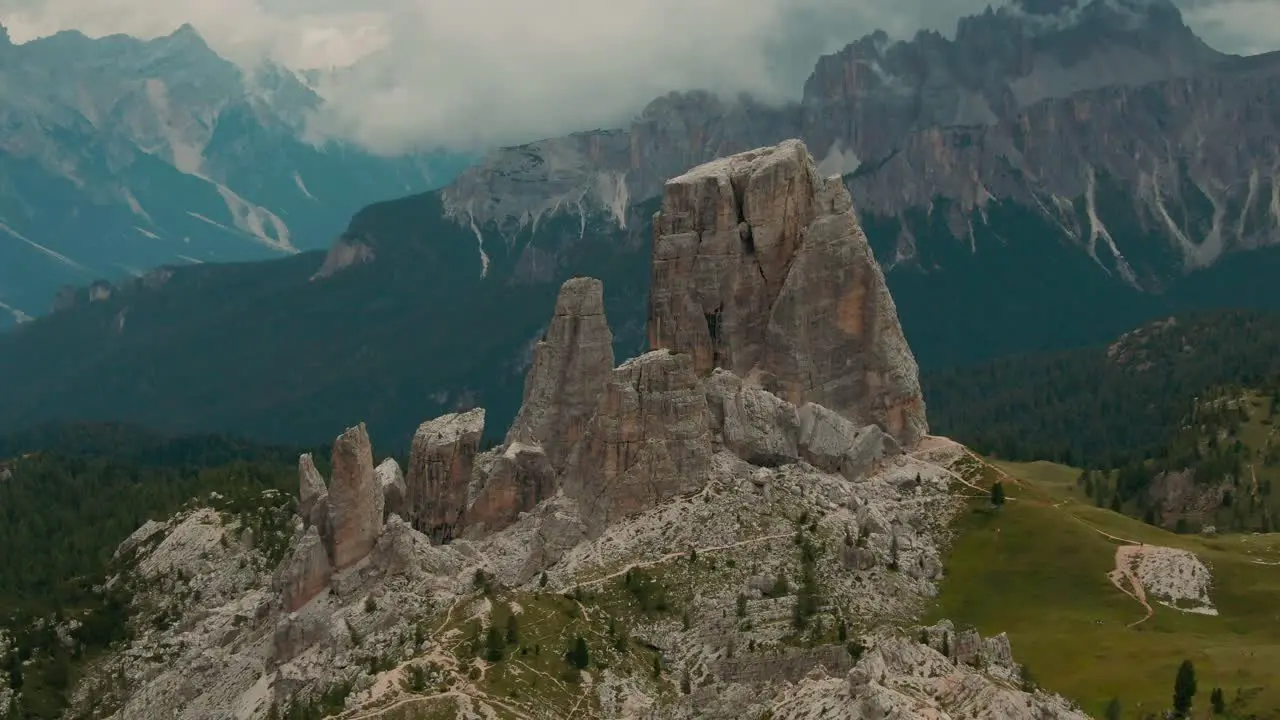 Tracking drone shot massive rock formations with distant tall mountains in the background green forest at the bottom cloudy day cinematic color grade