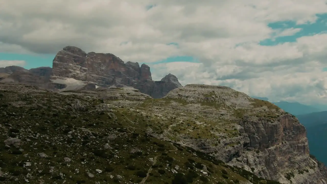 Drone shot with tall steep rocky mountains and partly clouded sky in the background cinematic color grade