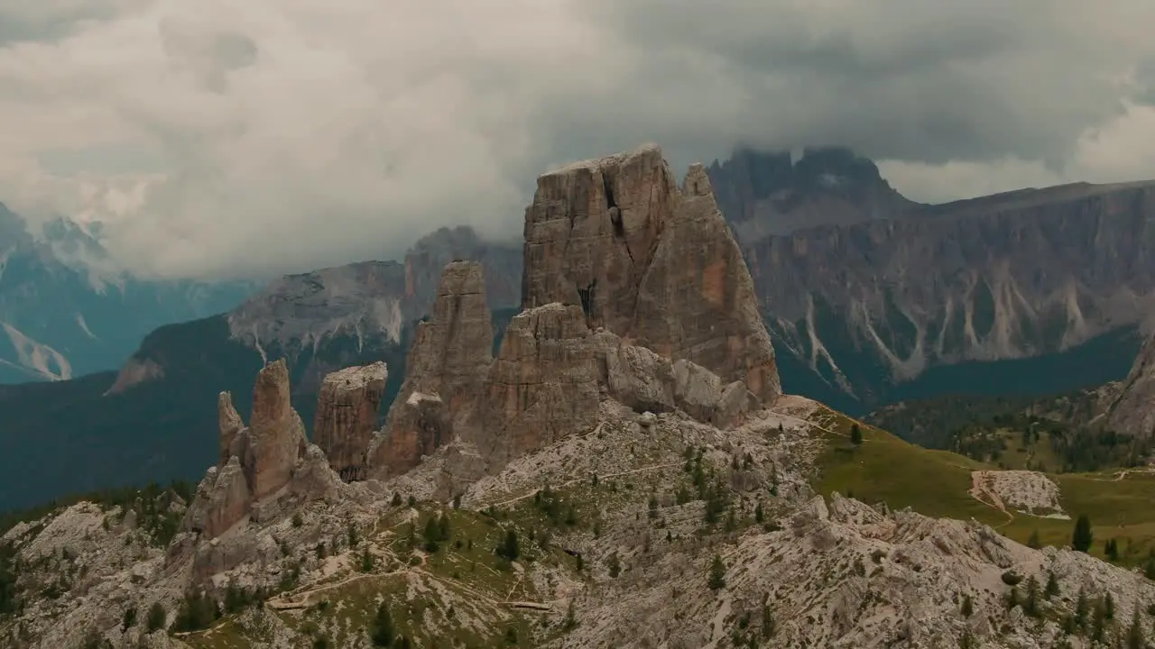 Parallax drone shot massive rock formations with distant tall mountains in the background green forest at the bottom cloudy day cinematic color grade