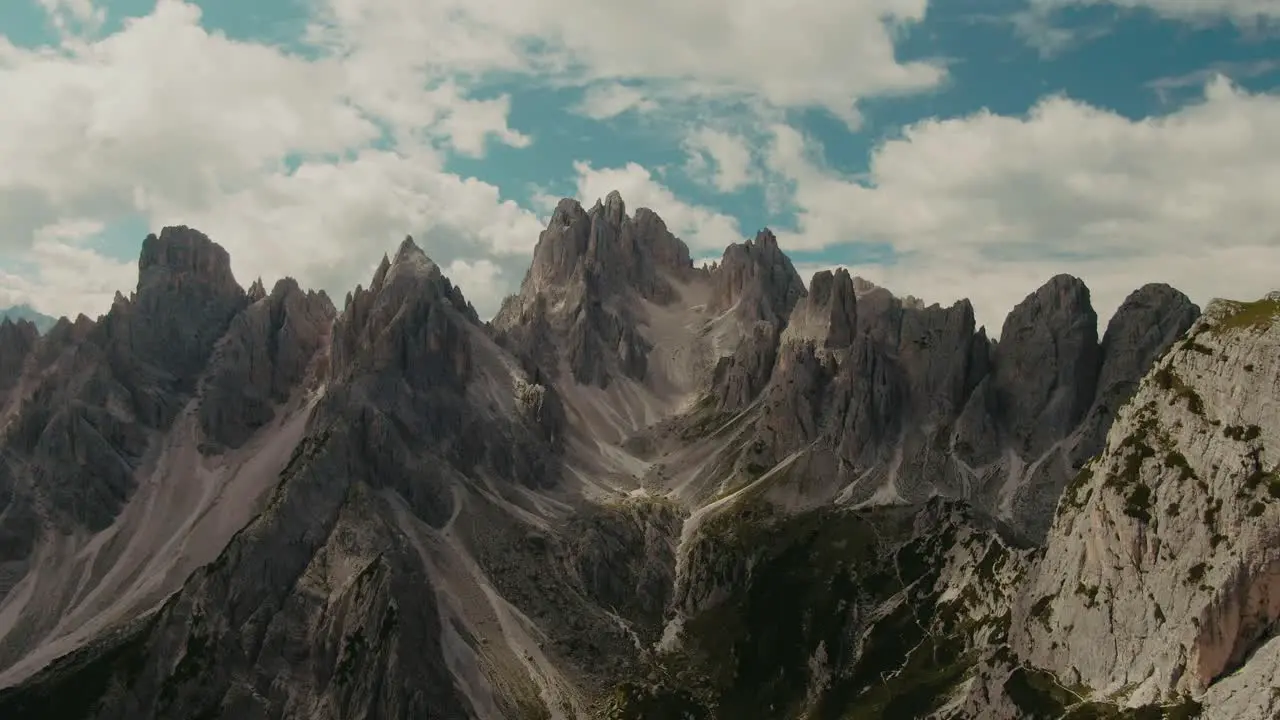 Drone shot with tall steep rocky mountains and partly clouded sky in the background hiking in the Alps majestic landscape cinematic color grade