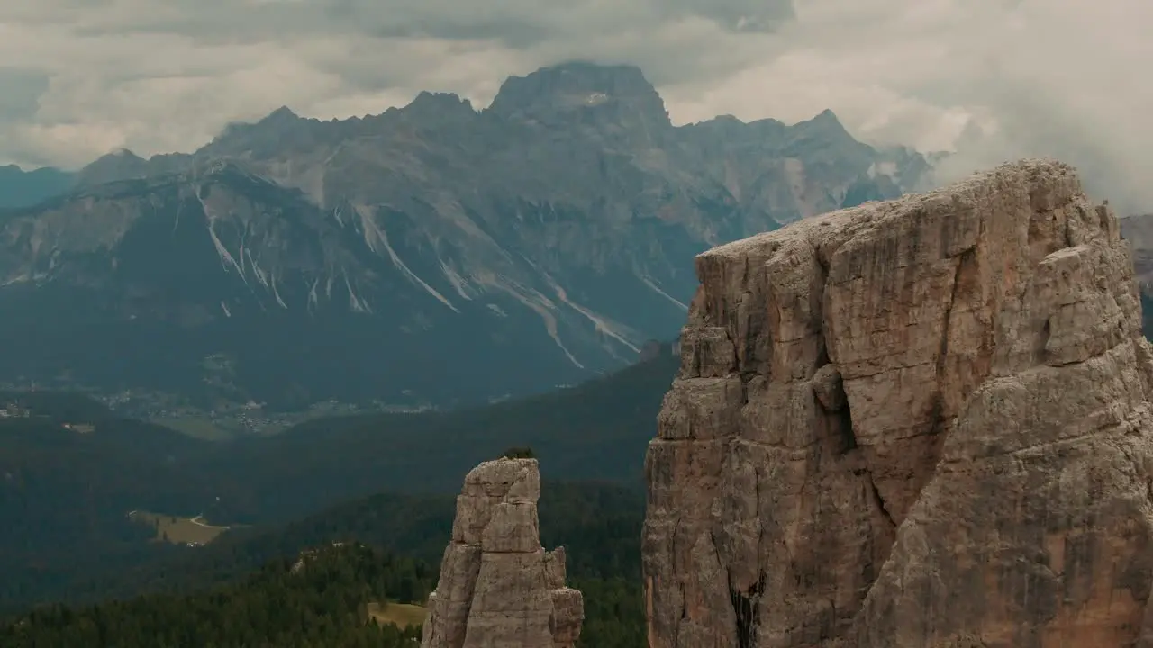 Aerial view flying past massive rocks to high mountains in the background green forest at the bottom cloudy day cinematic color grade