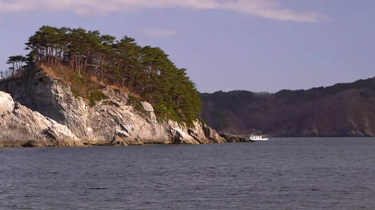 Small fishing vessel passing behind tall rock cliff and disappearing