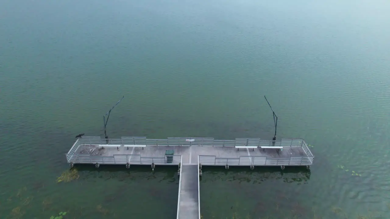 Flyover of fishing dock and aerial reveal of Starke Lake and cloudy sky in Ocoee Central Florida